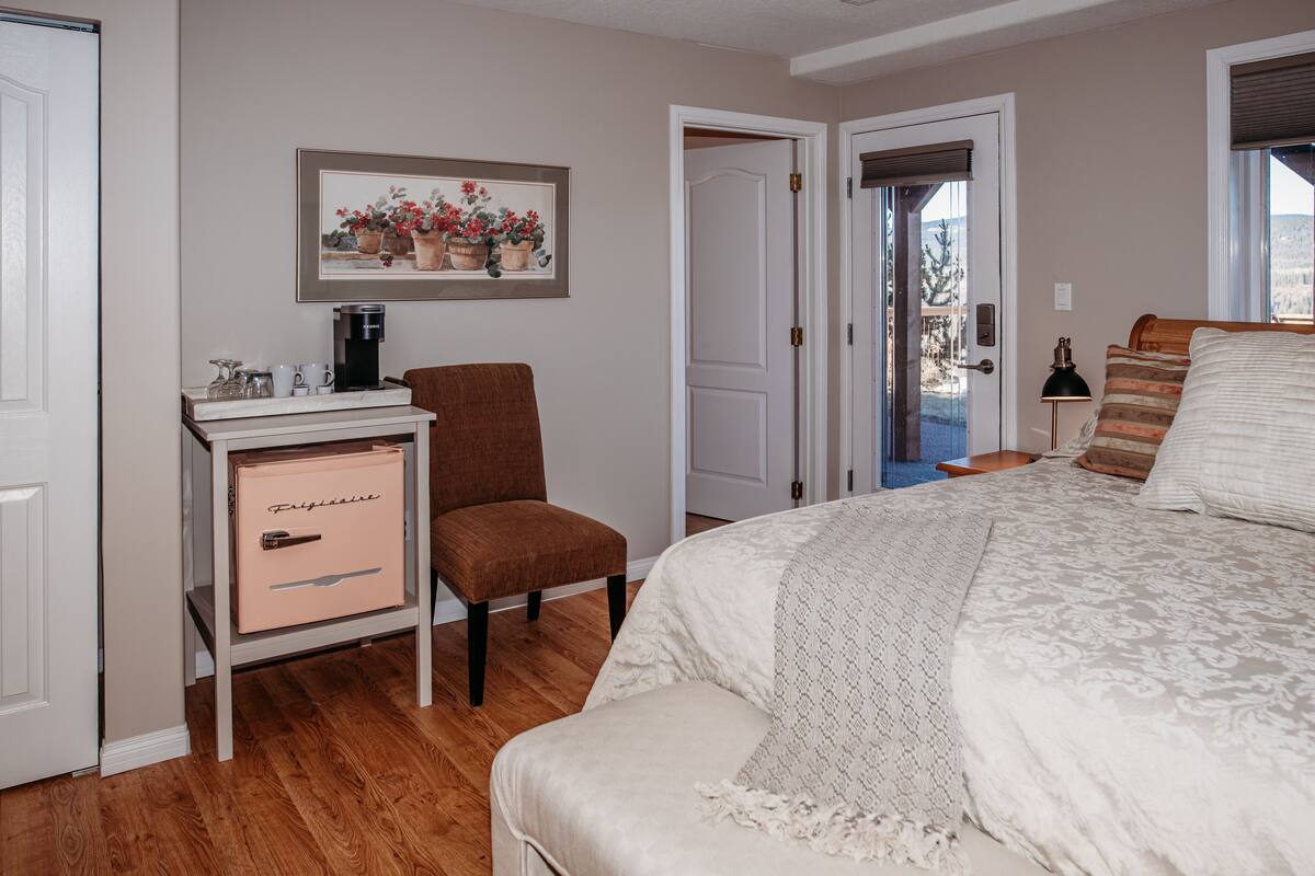 A bedroom with a bed, a chair, a dresser, a coffee maker, and a door leading to a balcony.