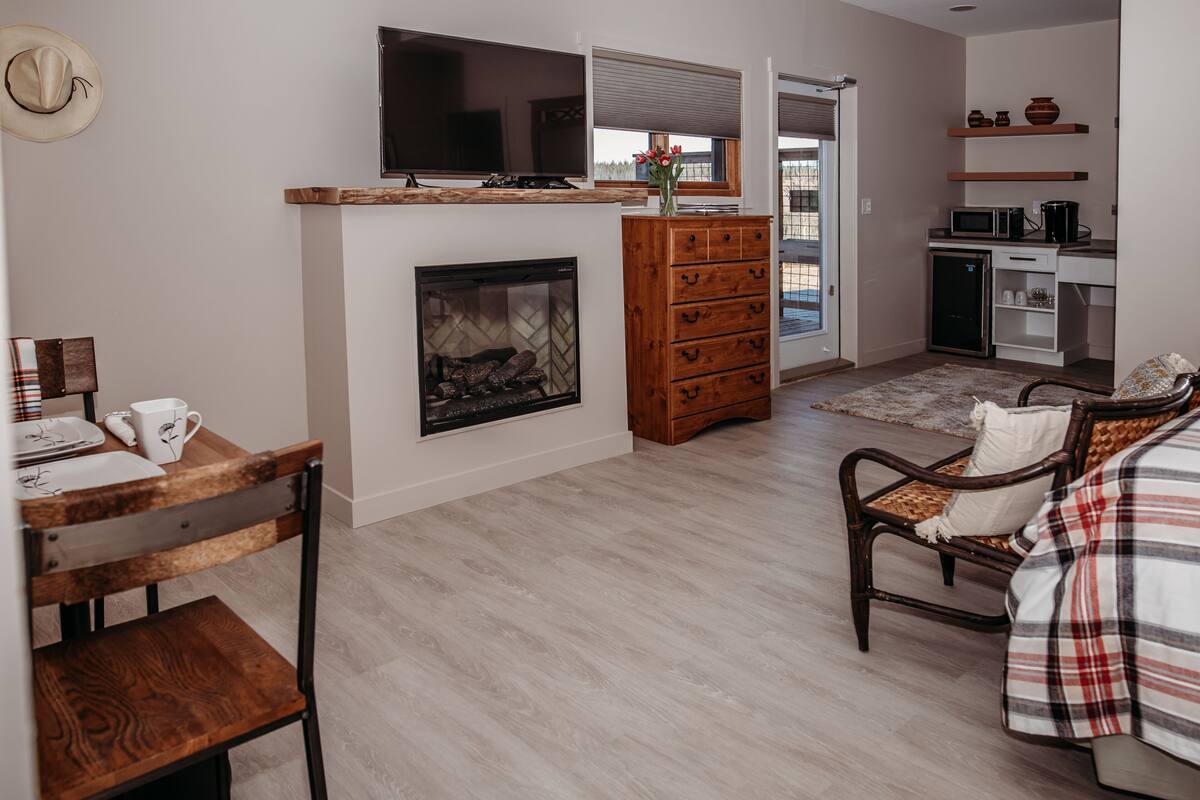 A modern living room with a fireplace, wooden furniture, a television, and a kitchen area with a microwave and cabinets.