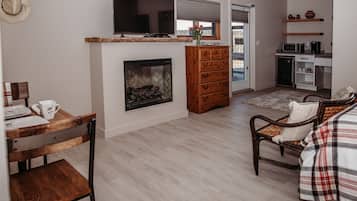 Una sala de estar moderna con chimenea, muebles de madera, televisor y una zona de cocina con microondas y armarios.