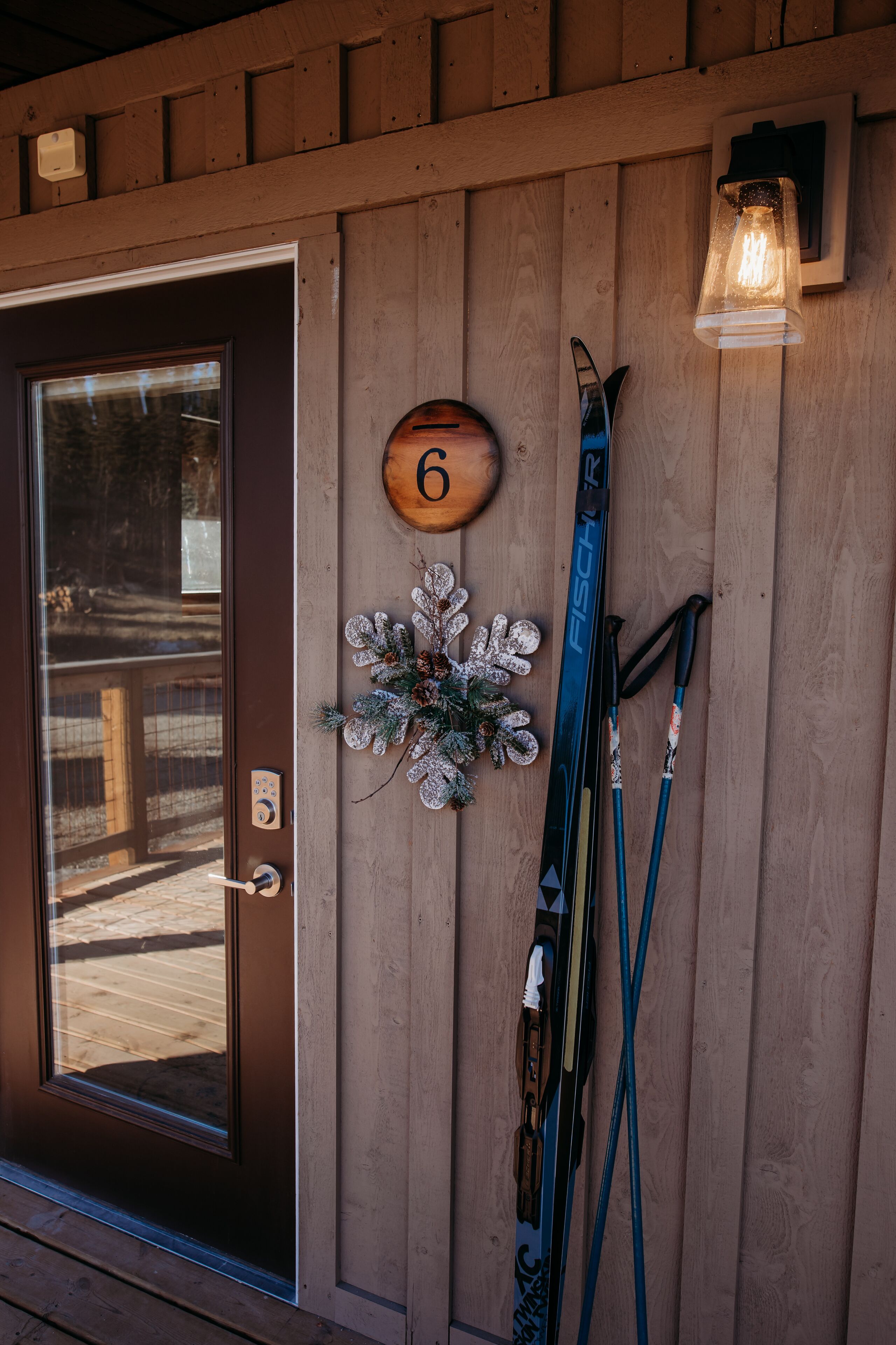 A wooden door with a number '6' sign, a decorative wreath, and skis leaning against the wall.