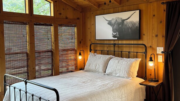 A wooden cabin bedroom with a bed, ceiling fan, and large windows.