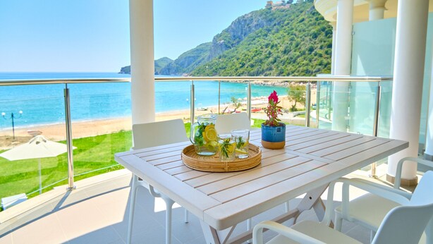 Ein Balkon mit Tisch für zwei Personen, Blick auf Strand und Berglandschaft.