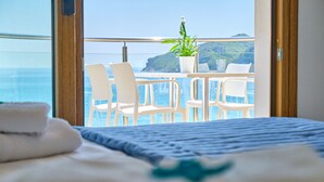 Ein Hotelzimmer mit Balkon und Meerblick, ein Bett mit blauer Bettdecke, weiße Stühle und ein Blumentopf.