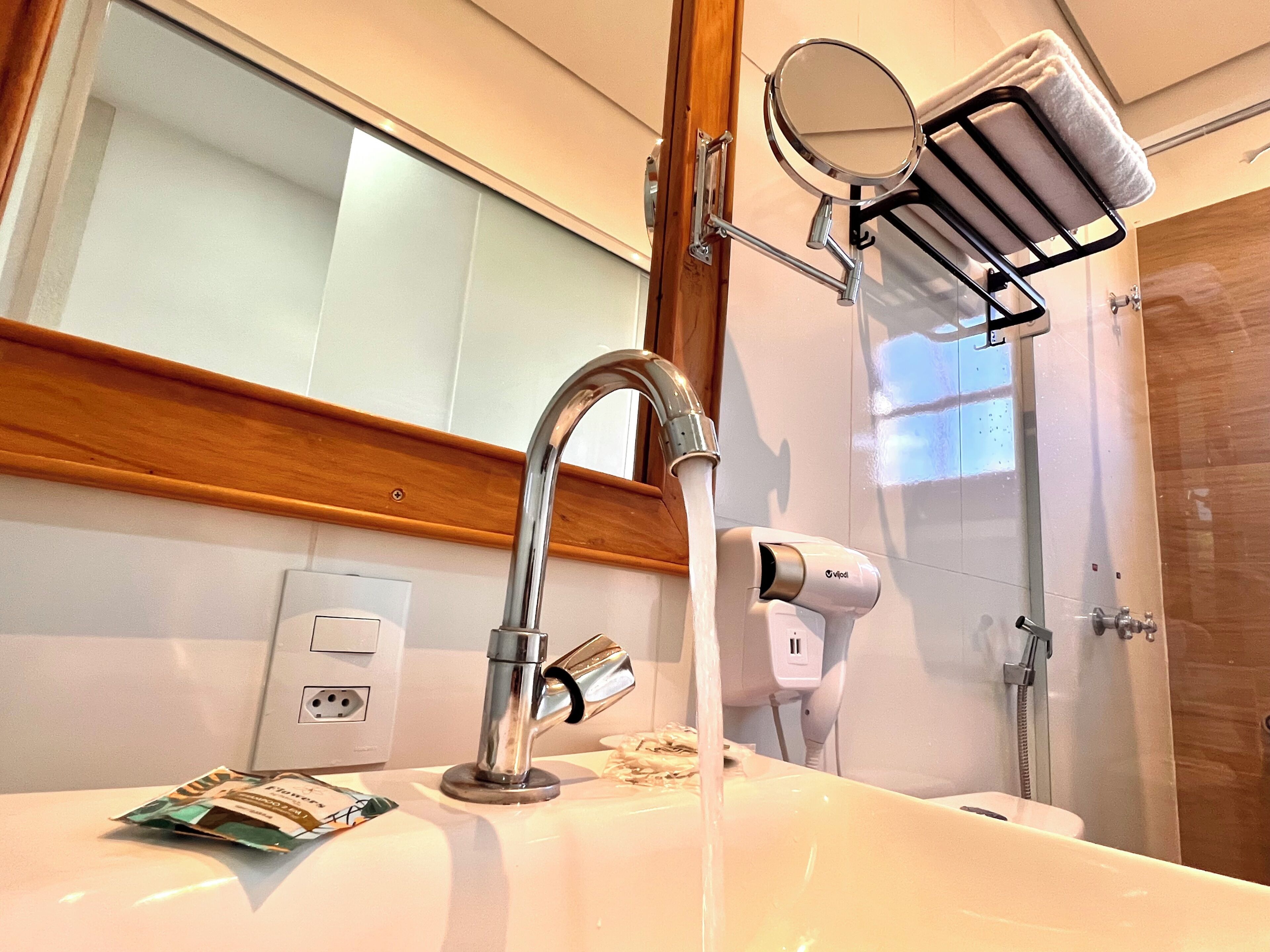 Une salle de bain équipée d’un lavabo, d’un miroir, d’un porte-serviettes, d’une douchette et d’un sèche-cheveux.