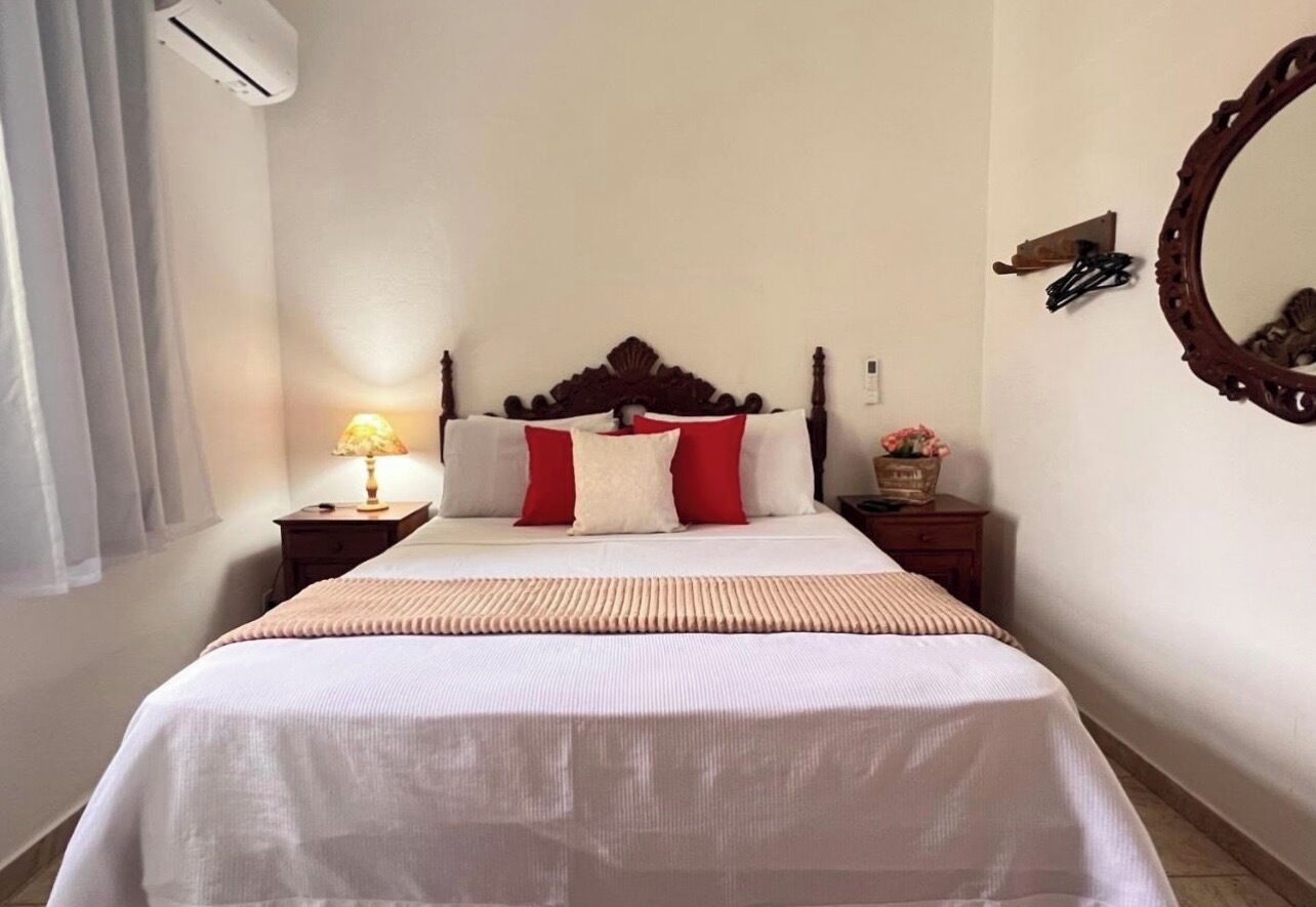 A hotel room with a bed, a nightstand, a lamp, a mirror, and a wall-mounted air conditioner.