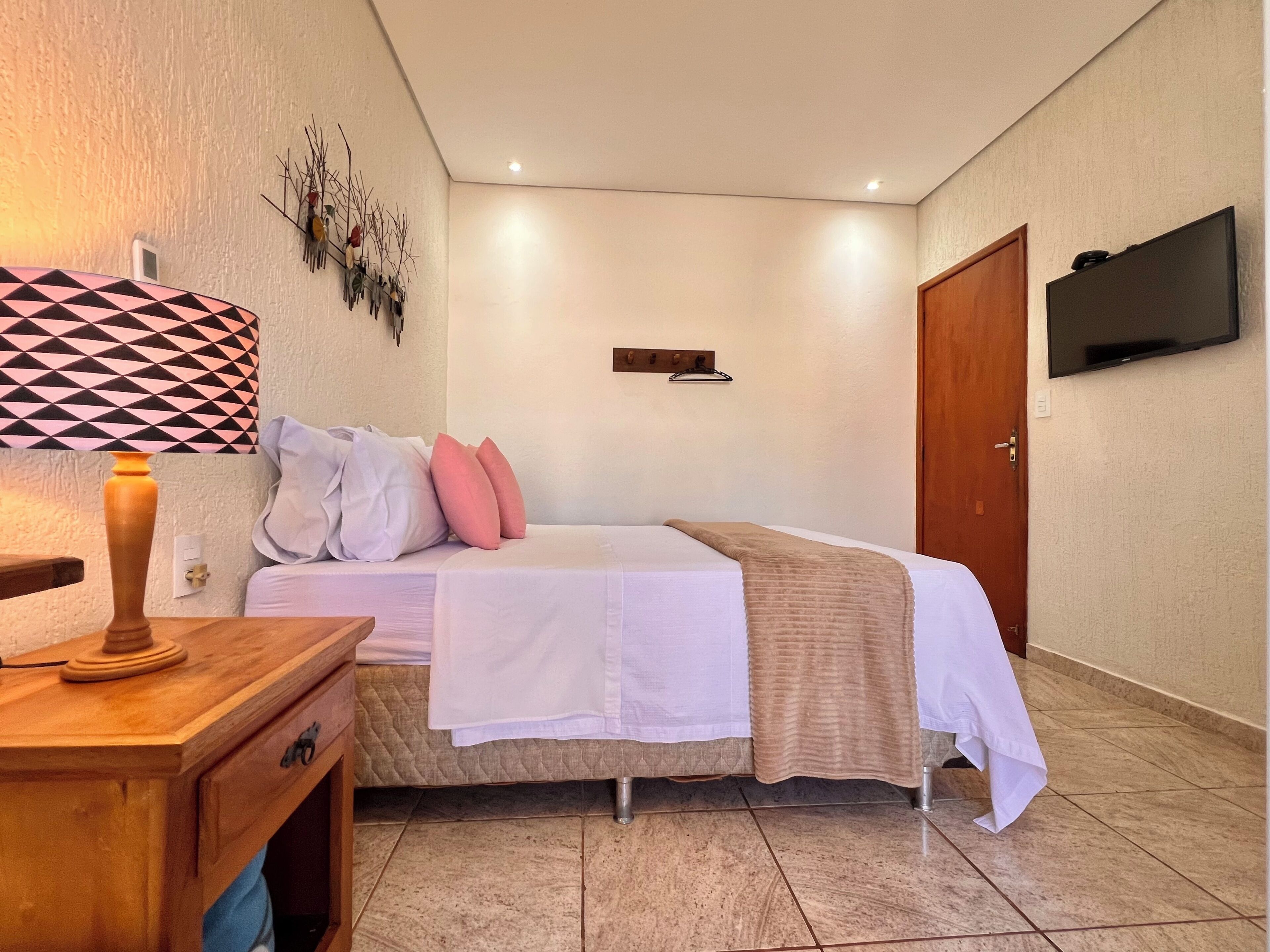 Een slaapkamer met een bed, nachtkastje, lamp, televisie aan de muur en een deur.