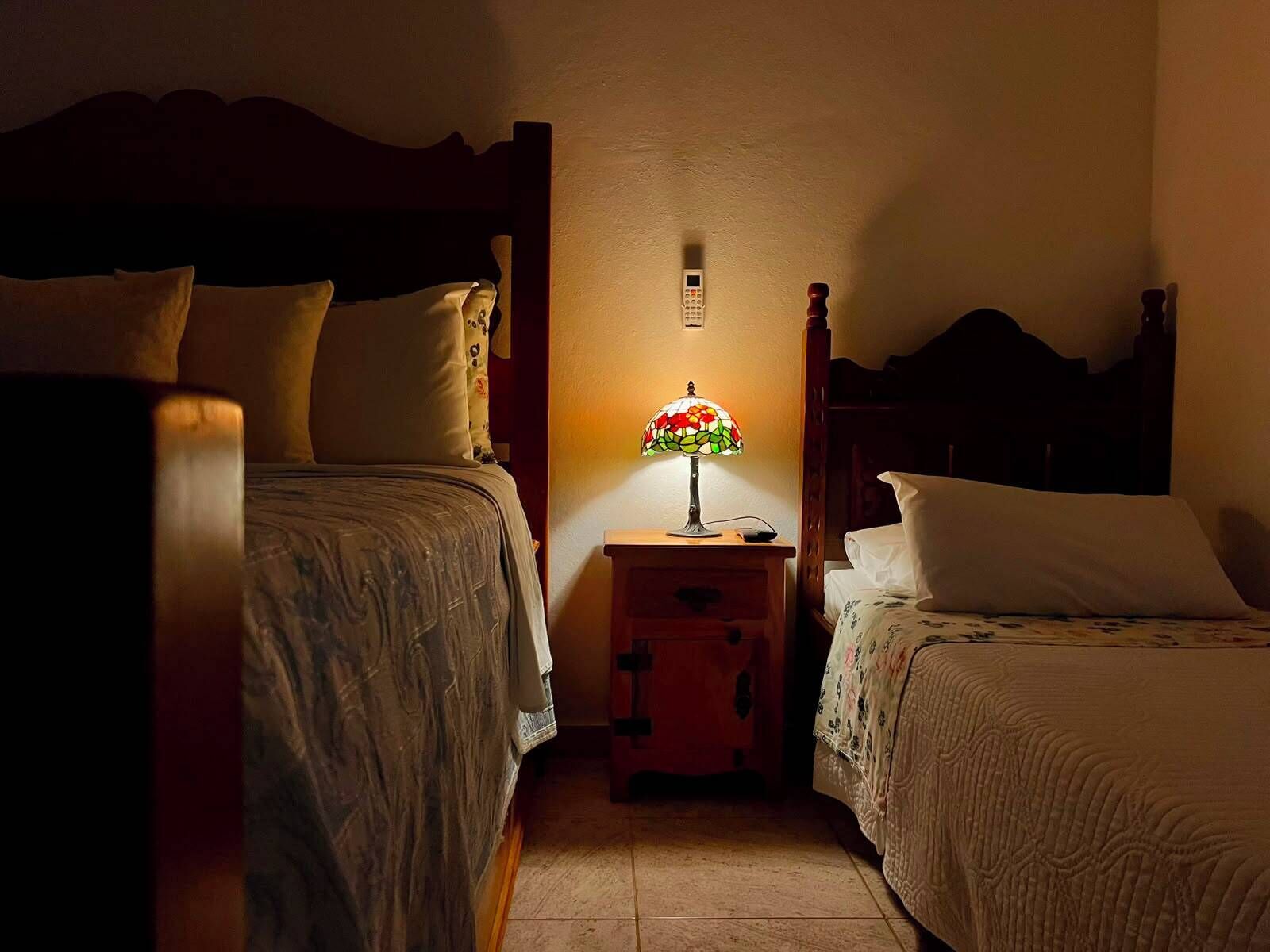 Un dormitorio con dos camas, una mesita de noche con lámpara y un despertador en la pared.