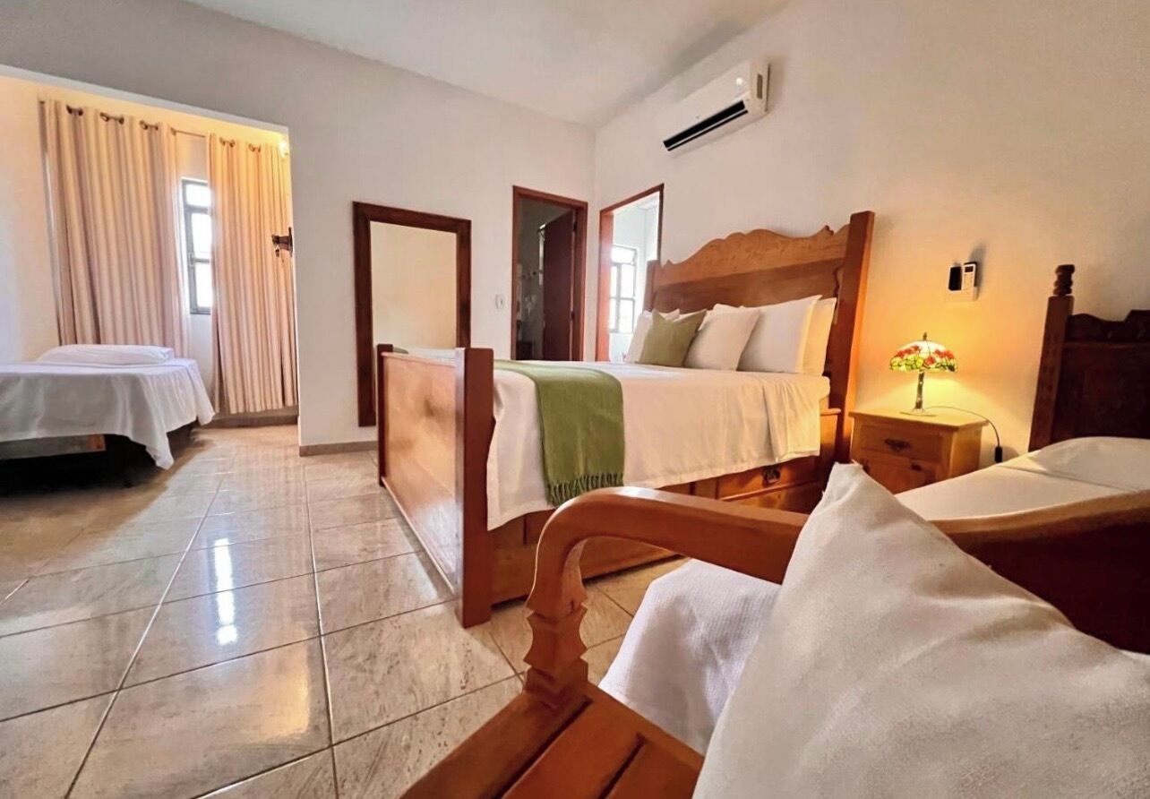 A hotel room with two beds, a wooden headboard, a bedside table with a lamp, and a window with curtains.