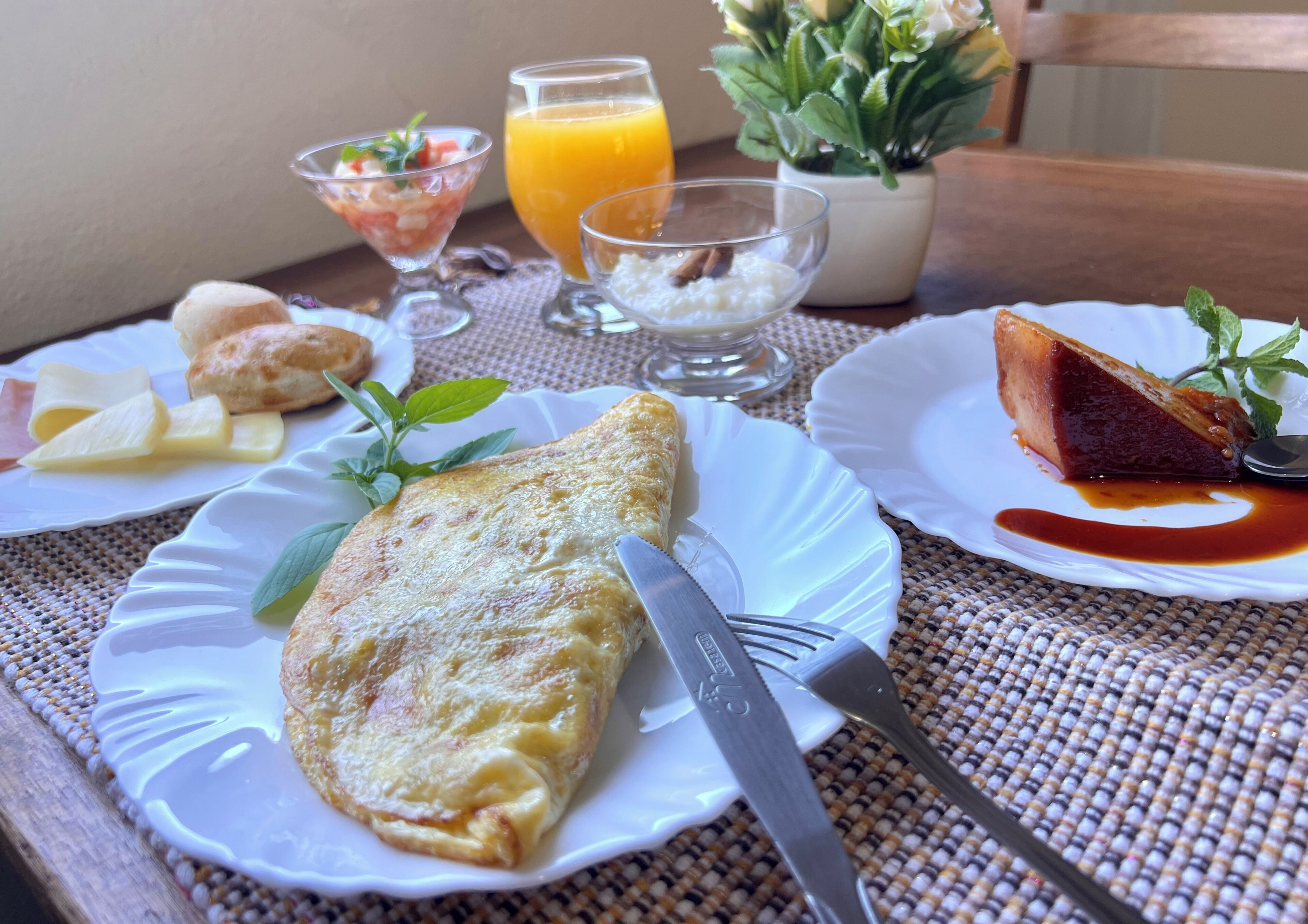 Una mesa con un plato de comida, un vaso de jugo de naranja, un tazón pequeño de arroz y una planta.