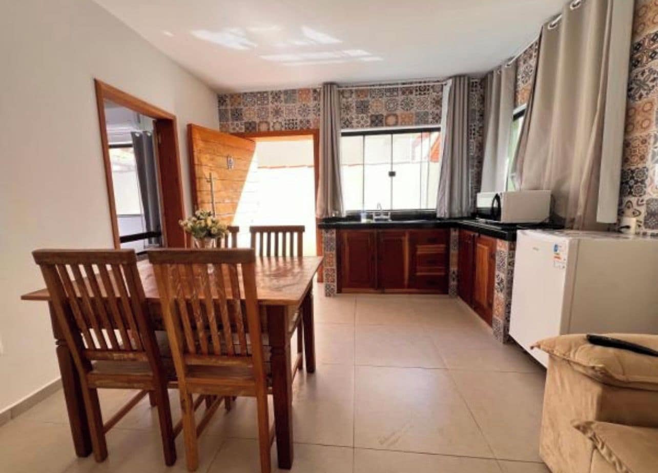 A compact kitchen with a dining area, a refrigerator, and a window with curtains.