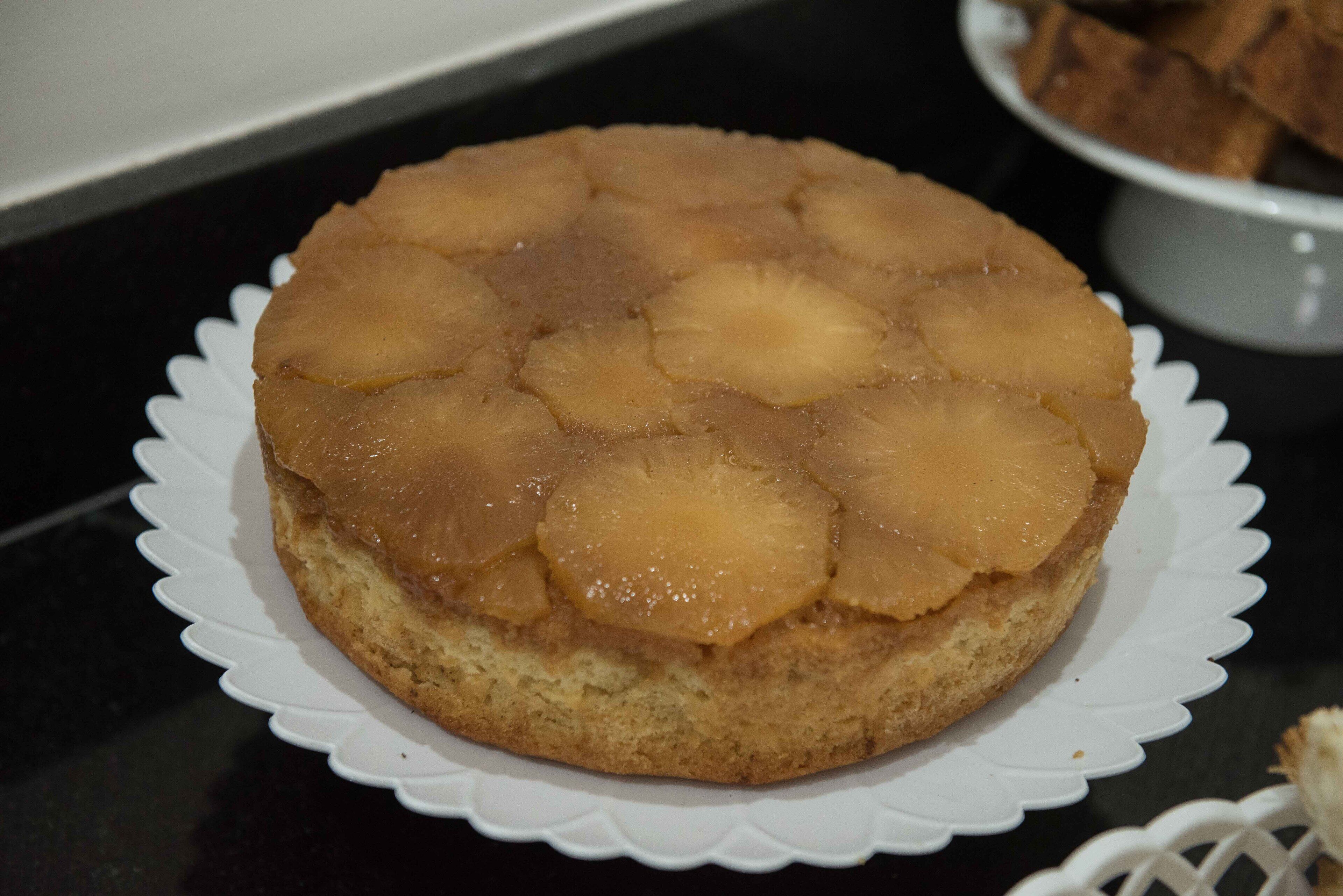 A round cake with pineapple slices on top, placed on a white plate with a scalloped edge.
