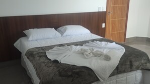 Una cama bien tendida con sábanas blancas y un cabecero marrón oscuro.
