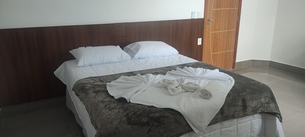 Una cama bien tendida con sábanas blancas y un cabecero marrón oscuro.