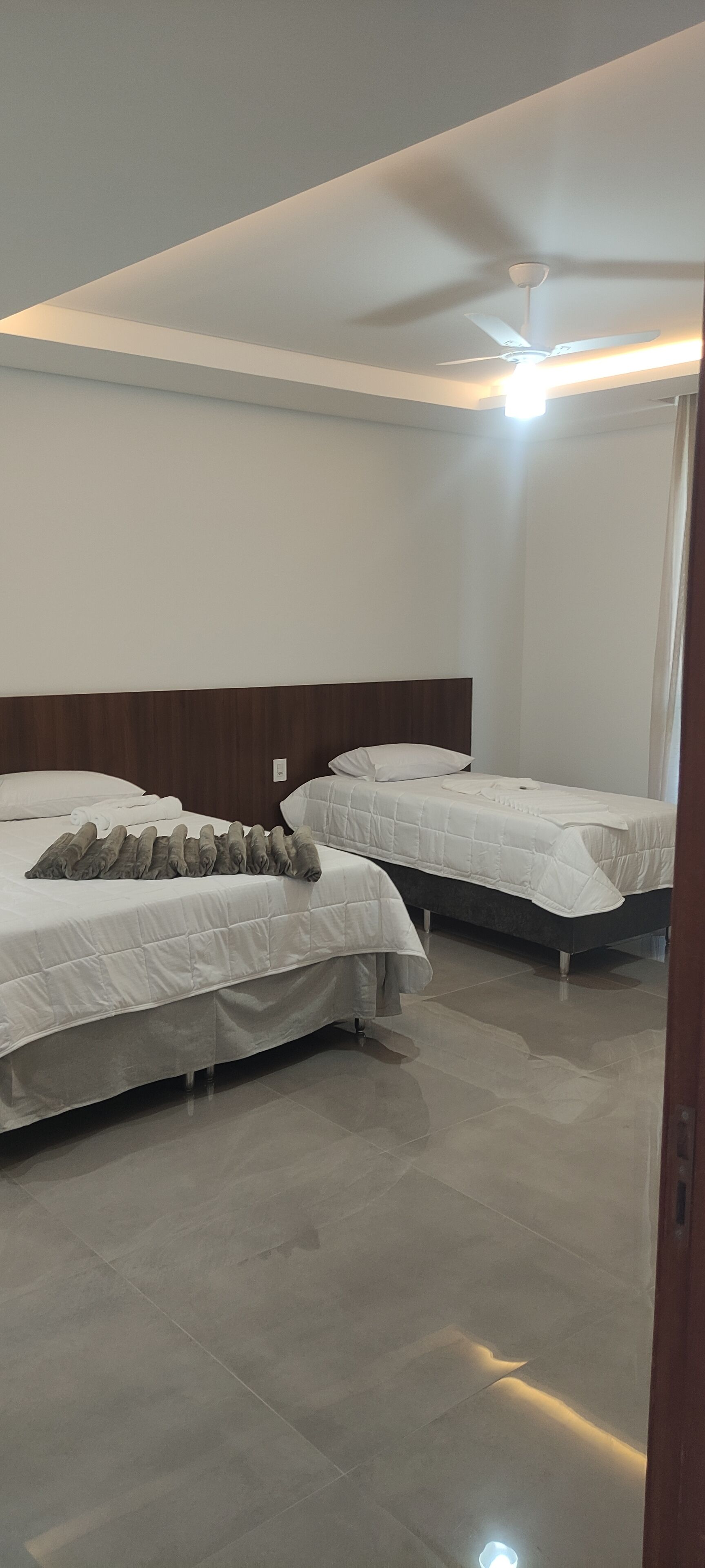 Habitación de hotel con dos camas, cabecero de madera y ventilador de techo.