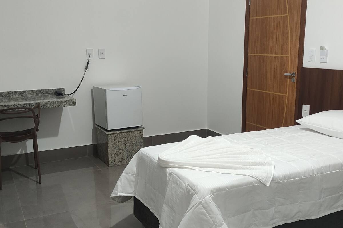 Een kleine, schone kamer met een bed, bureau en een koelkast.