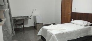Una habitación pequeña y limpia con cama, escritorio y refrigerador.