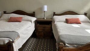 Dos camas individuales con cabeceros de madera, una mesita de noche con lámpara y un tapete estampado en el suelo.