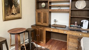 Un escritorio de madera con una silla, una mesita con un reloj y estantes con adornos.