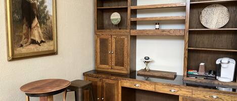 A wooden desk with a chair, a small table with a clock, and shelves with decorative items.