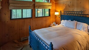Un dormitorio con techo de madera, una cama con cabecera azul y dos ventanas con cortinas.
