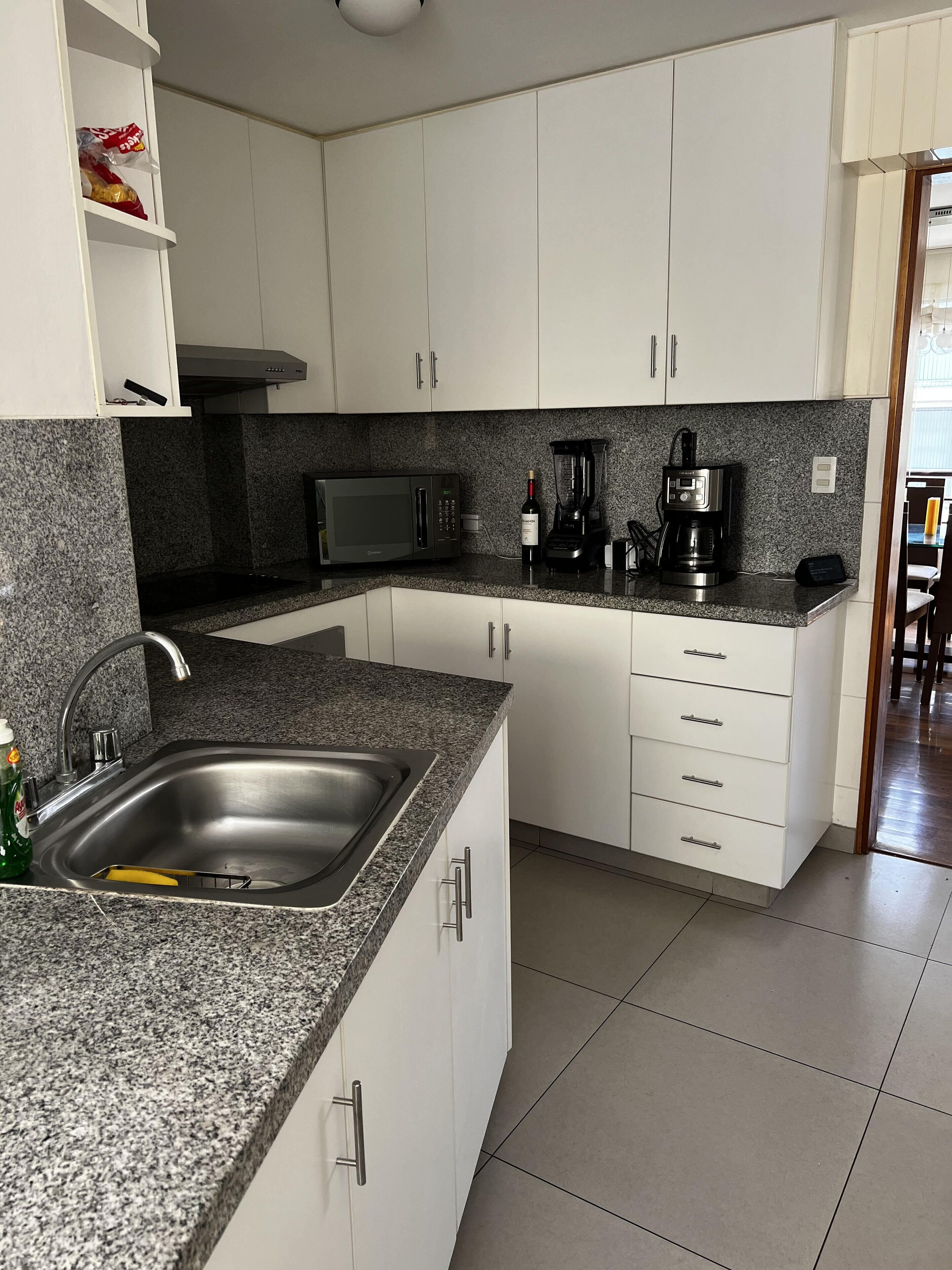 A kitchen with white cabinets, a granite countertop, a sink, a microwave, a blender, and a coffee maker.