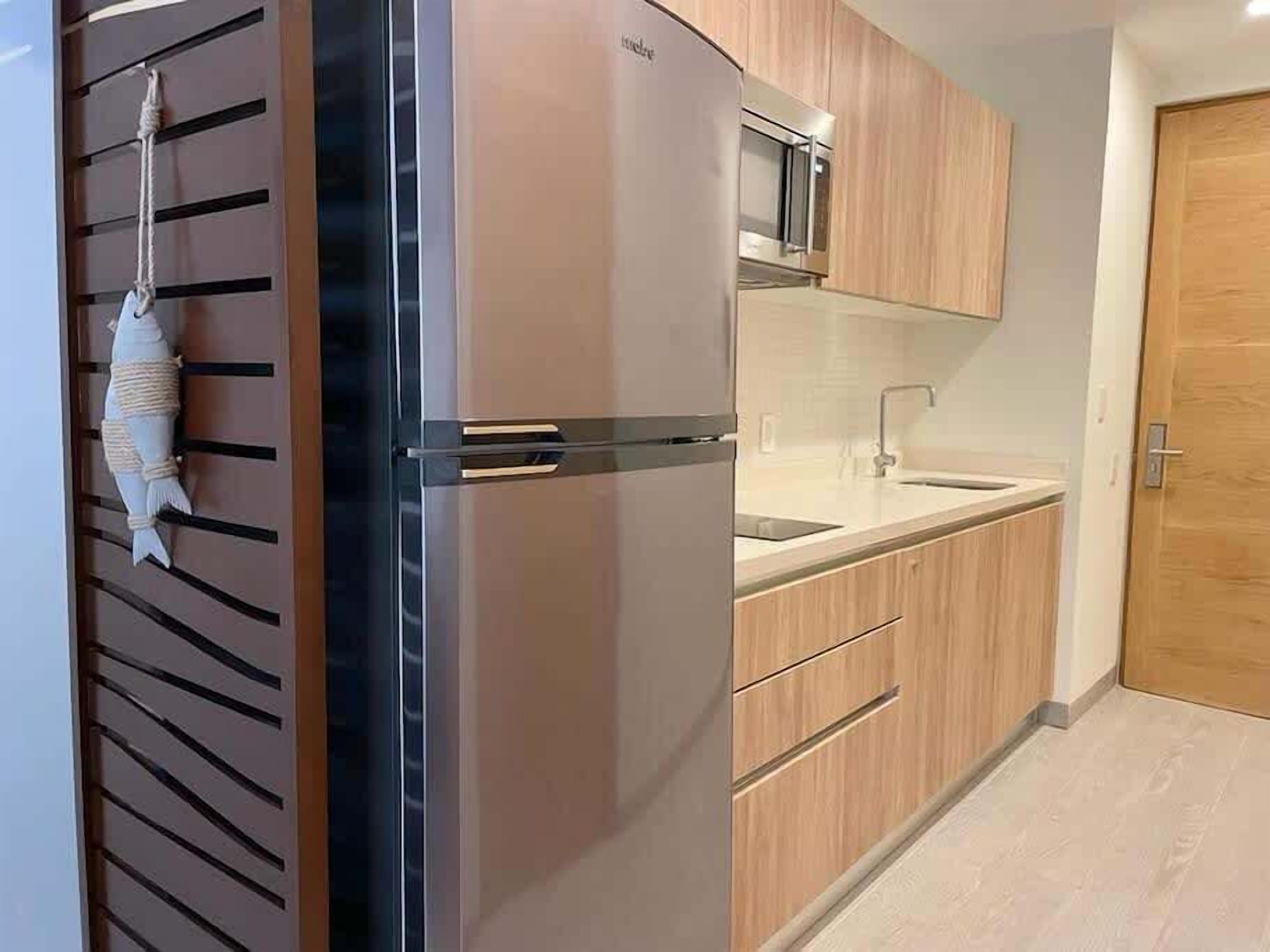 Une cuisine moderne équipée d’un réfrigérateur, d’un four à micro-ondes et de meubles de rangement en bois.