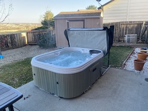 A hot tub in a backyard with a wooden deck, a shed, and a grassy area. - Spacious 3 BDR 2.5 BA House with Hot tub, BBQ, Fire Pit, Night View, Playground (Colorado Springs)