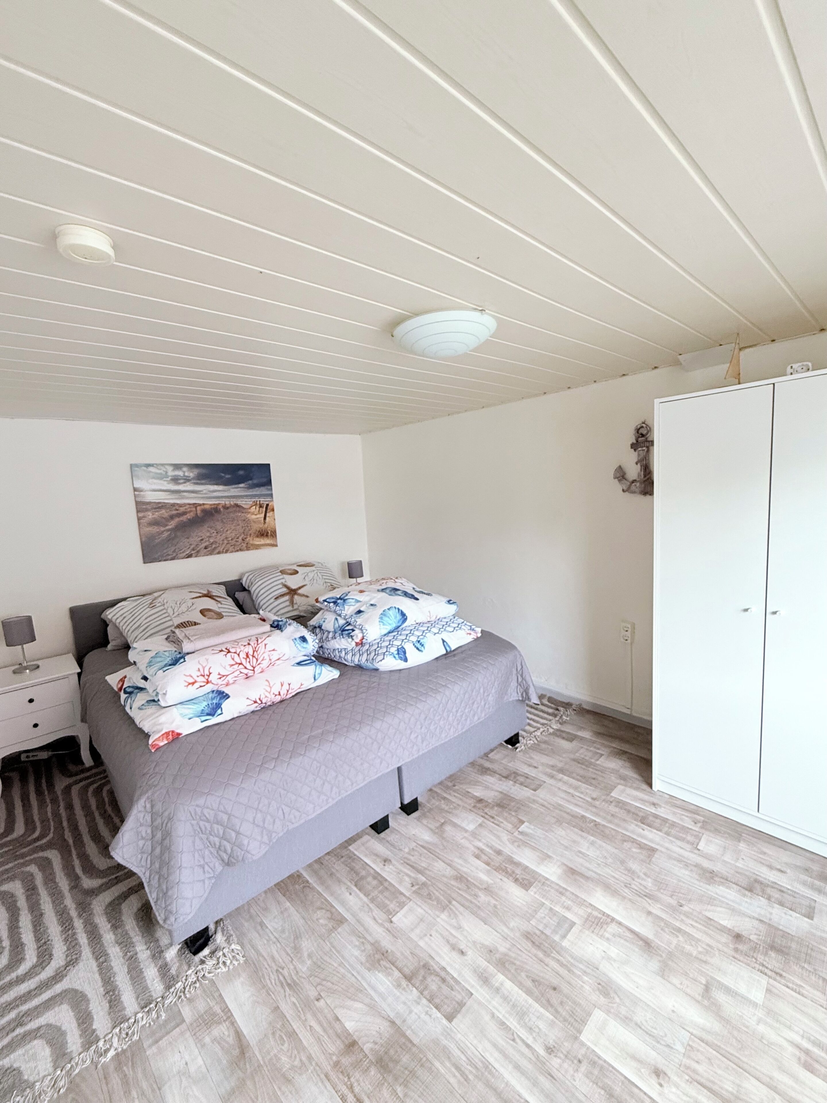 Une chambre à coucher comprenant un lit, une armoire, une table de chevet, une lampe et un luminaire au plafond.