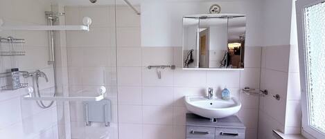 A modern bathroom with a glass shower enclosure, a white sink, and a vanity with drawers.