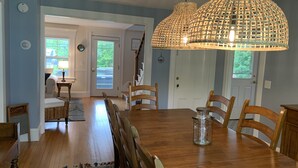Uma sala de jantar com uma mesa e cadeiras de madeira, um pendente de luz tecido e vista para o exterior através de uma porta.