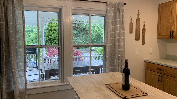 Uma cozinha com uma mesa de madeira, uma garrafa de vinho e vista para uma varanda com vegetação.