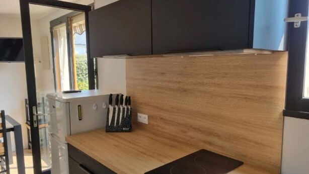 Une cuisine de taille réduite, dotée d’un plan de travail en bois, d’un range-couteaux et d’une fenêtre agrémentée de rideaux.
