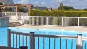 Une piscine entourée d’une clôture blanche, avec une pergola en arrière-plan.