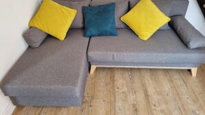Un canapé d’angle gris avec deux coussins jaunes et un coussin bleu, placé contre un mur blanc.
