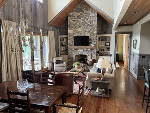 A spacious living area with a stone fireplace, wooden ceiling, and a cozy seating arrangement.