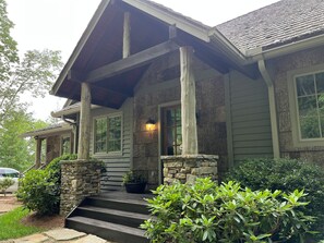 A house with a stone foundation, wooden steps, and a porch with a stone column.