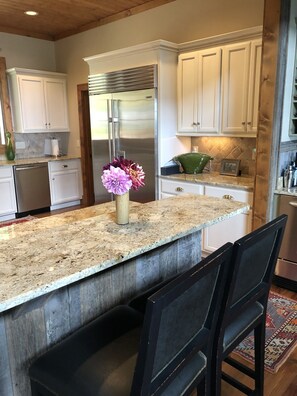 A kitchen with white cabinets, a stainless steel refrigerator, a granite countertop, and a vase with flowers.