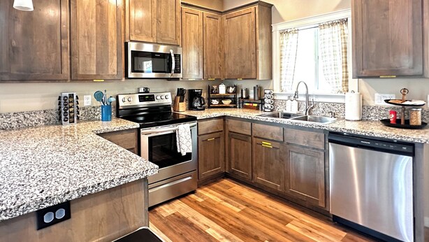 A modern kitchen with wooden cabinets, stainless steel appliances, granite countertops, and a wood floor. - Charming 2BR Cottage • Near Freeway-Cul-de-sac (Medford)