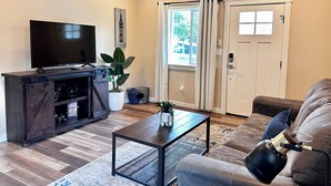 A living room with a TV, a coffee table, a sofa, and a ceiling fan. - Charming 2BR Cottage • Near Freeway-Cul-de-sac (Medford)