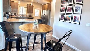 A modern kitchen with granite countertops, stainless steel appliances, and a dining area with a round wooden table and black chairs. - Charming 2BR Cottage • Near Freeway-Cul-de-sac (Medford)