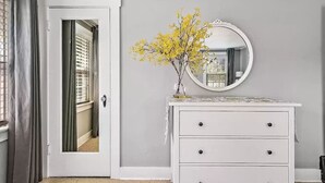 A room with a white dresser, a round mirror, and a vase with yellow flowers.