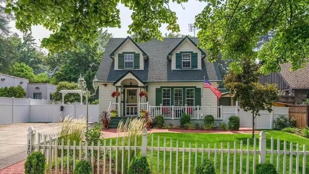 A two-story house with a front porch, green shutters, and a white picket fence.