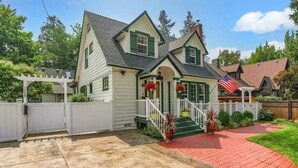 A two-story house with a front porch, a white fence, and a red brick pathway.