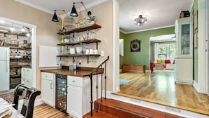 A kitchen with wooden shelves, a dining area with a table and chairs, and a staircase leading to a living room.
