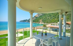 Un espacio de estar al aire libre cubierto con una mesa y sillas, con vista a una playa y un paisaje montañoso.