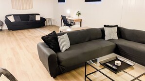 En moderne stue med en sort sofa, et glasbord og et spiseområde i baggrunden.
