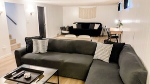 En moderne stue med en hjørnesofa, et sofabord og et spiseområde med bord og stole.