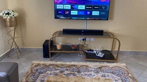 A living room with a flat-screen TV mounted on the wall, a coffee table with a decorative rug, and a side table with a vase of flowers. - Stunning 2-bed Cozy Furnished Apartment in Nairobi (Nairobi)