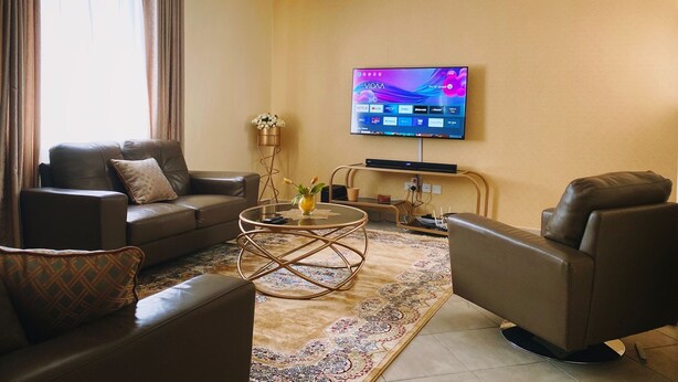 A modern living room with a sofa, armchair, coffee table, and a flat-screen TV mounted on the wall. - Stunning 2-bed Cozy Furnished Apartment in Nairobi (Nairobi)