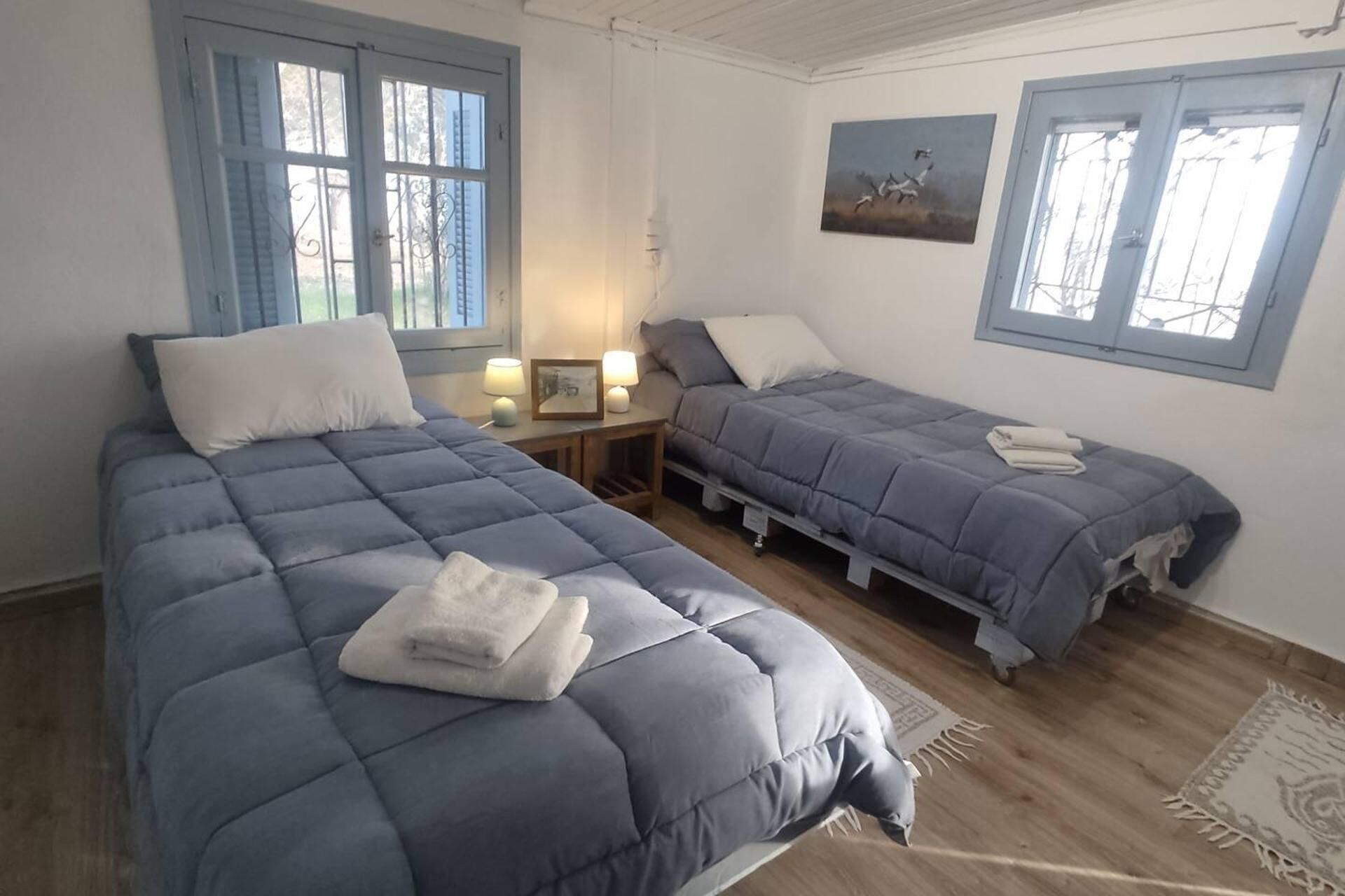 Habitació amb dos llits, cadascun amb un edredó blau i nínxols blancs, una petita taula de nit amb una làmpada i un quadre encimbellat a la paret.